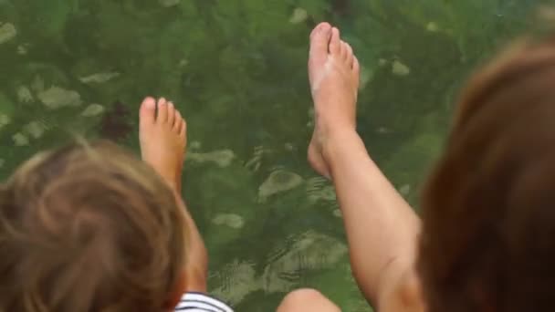 Slowmotion steadycam tiro de mulher e seu filho se divertindo sentado em uma passarela de madeira sobre um mar — Vídeo de Stock