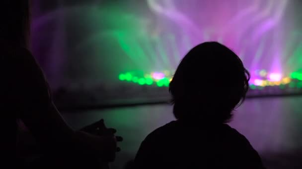 Moeder en zoon kijken naar een kleurrijke dansende fontein show. Vrouw kussen haar zoon — Stockvideo