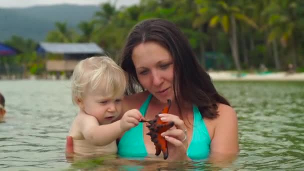 Fotografía en cámara lenta de una mujer y su pequeño hijo jugando con estrellas de mar rojas en una playa — Vídeos de Stock