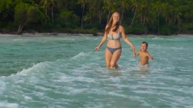 Güzel genç bir kadın ve oğlu eğleniyor bir plaj ve deniz Slowmotion atış