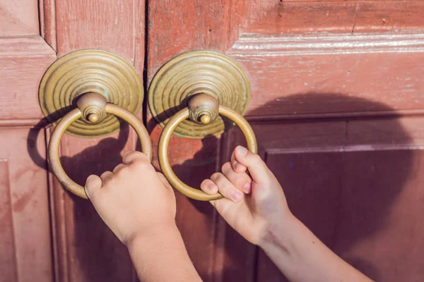 The hand opens the antique door by the round handle.