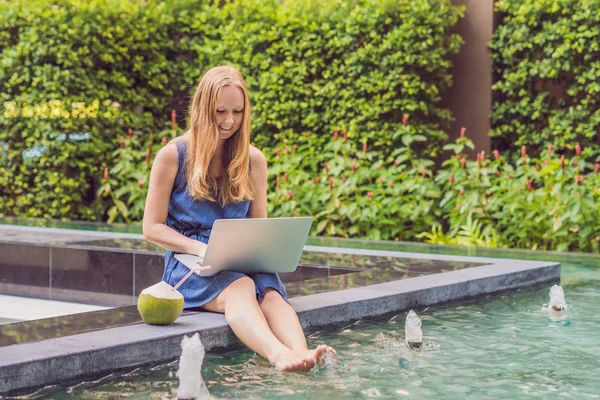 그녀의 스마트폰에 브라우징 호텔에서 그녀의 노트북으로 수영장 근처에 앉아있는 프리랜서 — 스톡 사진