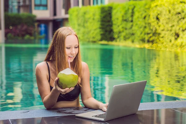 Young female freelancer sitting near the pool with her laptop in the hotel browsing in her smartphone. Busy at holidays. Distant work concept. Copy space for your text.