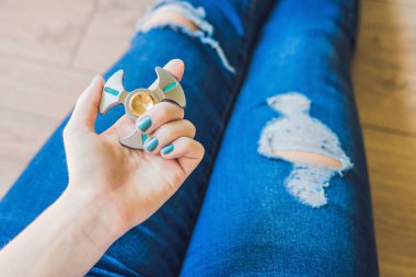 Girl teenager in holey jeans holds in hands and plays with spinner. clipart