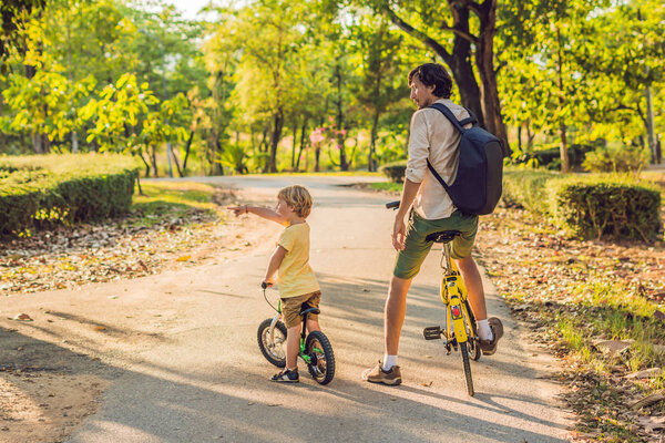Отец и сын катаются на велосипедах и улыбаются
