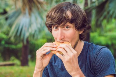 Genç adam parkta bir hamburger yeme
