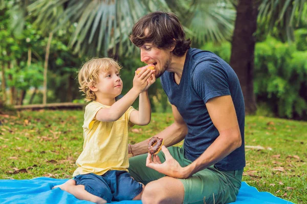 お父さんと息子は 公園で ドーナツを食べています 家族に有害な栄養 — ストック写真