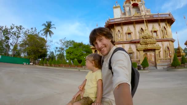 Fotografía en cámara lenta de un joven y su hijo haciendo selfie en fron de un templo budista de Wat Chalong en la isla de Phuket, Tailandia — Vídeos de Stock