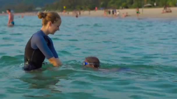 Mujer instructora de natación enseña a niño a nadar en un mar durante un atardecer — Vídeo de stock