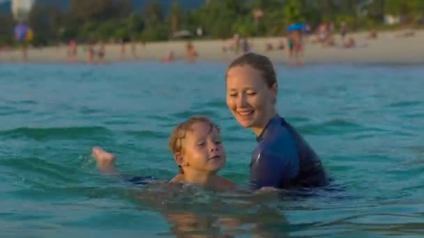 Woman swimming instructor teaches little boy swimming in a sea during a sundet — Stock Video