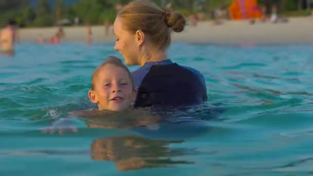 Woman swimming instructor teaches little boy swimming in a sea during a sundet — Stock Video
