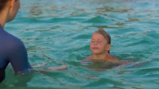 Woman swimming instructor teaches little boy swimming in a sea during a sundet — Stock Video