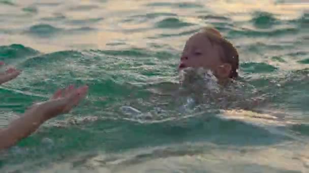 Mujer instructora de natación enseña a niño a nadar en un mar durante un atardecer — Vídeo de stock