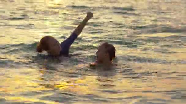 Une femme instructrice de natation enseigne à un petit garçon à nager dans une mer pendant un coucher de soleil — Video