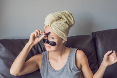 Güzel genç kadın ile yüz maskesi güzellik Spa'da rahatlatıcı. Yüzünde siyah maske uygulayarak mutlu neşeli kadın.