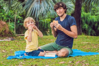 Genç bir baba ve oğlu bir hamburger bir parkta zevk ve gülümseyen portresi.