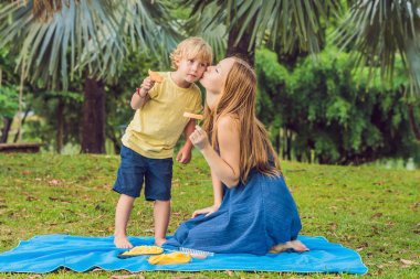 Anne ve oğlu Parkta piknik. Sağlıklı meyve - mango, ananas ve kavun yemek. Çocuk sağlıklı yemek yeme