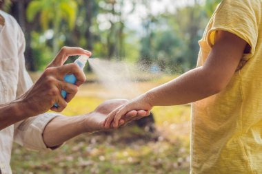 dad and son use mosquito spray.Spraying insect repellent on skin outdoor. clipart