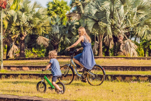 Happy family is riding bikes outdoors and smiling. Mom on a bike and son on a balancebike.