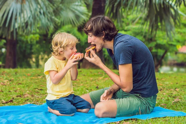 Papa et fils mangent un beignet dans le parc. Nutrition nuisible dans la famille — Photo