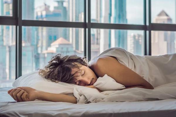 Man wakes up in the morning in an apartment in the downtown area with a view of the skyscrapers. Life in the noise of the big city concept. Not enough sleep.