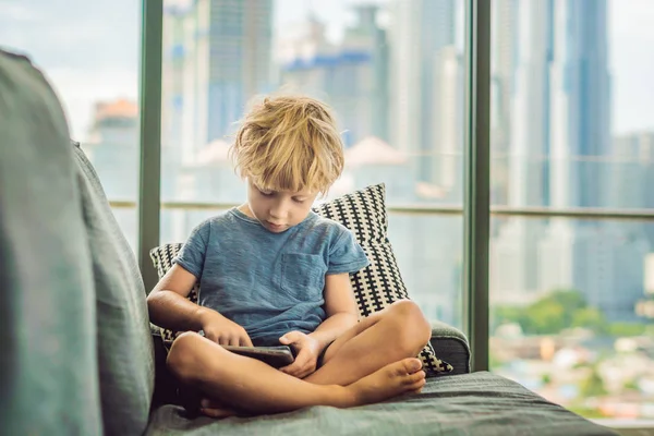 Boy Utiliza Una Tableta Casa Sofá Fondo Ventana Con Rascacielos — Foto de Stock