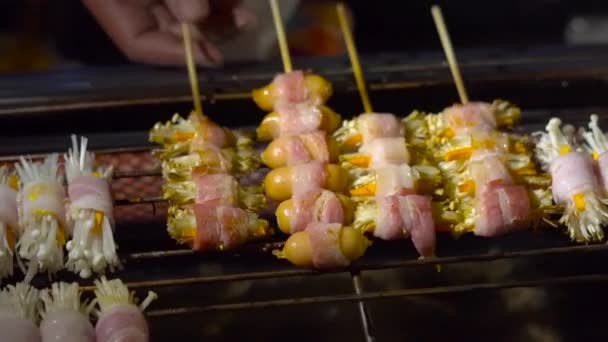 Proces van het maken van barbecue van een paddestoelen verpakt in een spek op een avondmarkt in Thailand. Thais eten concept. Aziatisch eten concept — Stockvideo