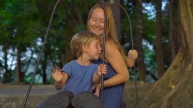 Anne ve oğlu tropikal bir parkta büyük bir tropik ağaç üzerinde asılı bir egzotik eski hali üzerine salıncak. Çocuklar kavramı ile seyahat