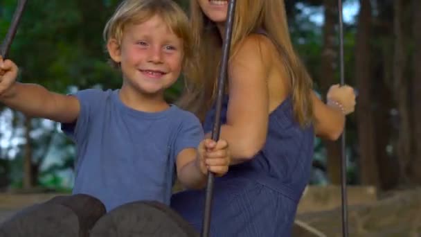 Mor och son gunga på en exotisk gamla gungor hängande på en stora tropiska träd i en tropisk park. Resa med kids concept — Stockvideo