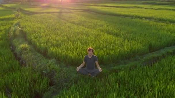 Tiro aéreo de um homem meditando em um maravilhoso campo de arroz durante o pôr-do-sol — Vídeo de Stock