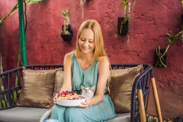 Mujer joven tomando un desayuno mediterráneo sentada en su sofá y con su gato y come desayuno tropical saludable, batido con frutas tropicales, decorado con un patrón de yogur colorido — Foto de Stock