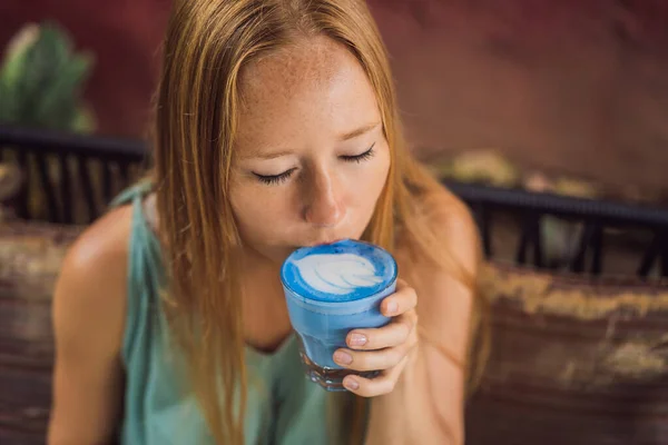 지중해 아침 식사를 하고 있는 젊은 여성 이 소파에 앉아 트렌디 음료를 마시고 있습니다. 파란 라떼입니다. 뜨거운 나비 완두콩 혹은 푸른 스피룰리나 라테 — 스톡 사진