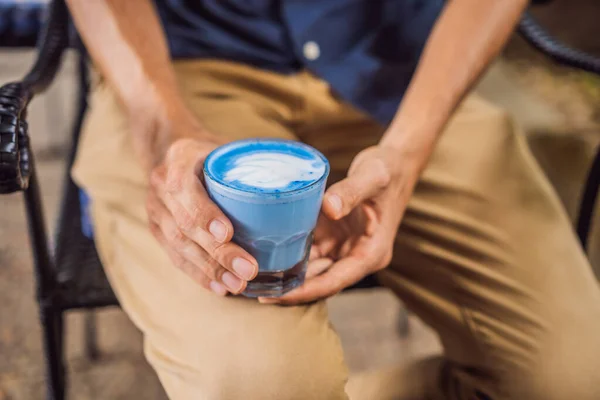 Νεαρός που τρώει μεσογειακό πρωινό καθισμένος σε καναπέ και ποτά Μοντέρνο ποτό: Blue latte. Καφές με καυτό μπιζέλι πεταλούδα ή μπλε σπιρουλίνα λάτε — Φωτογραφία Αρχείου