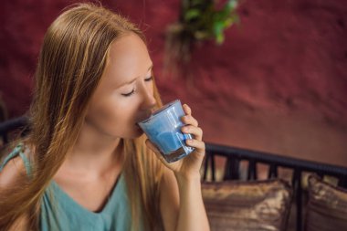 Akdeniz kahvaltısı yapan genç bir kadın kanepede oturuyor ve Moda içeceği olan mavi latte içiyor. Sıcak kelebek bezelye latte veya mavi spirulina latte.