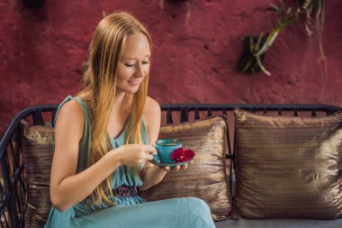 Genç bir kadın kanepede oturmuş Akdeniz kahvaltısı yapıyor ve sıcak aromatik kahve içiyor.