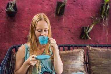 Genç bir kadın kanepede oturmuş Akdeniz kahvaltısı yapıyor ve sıcak aromatik kahve içiyor.