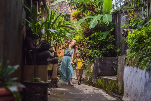 バリ島の母親と息子の観光客は、ウブドの狭い居心地の良い通りを歩いています。バリ島は人気のある観光地です。バリの概念への旅行。子供と一緒に旅行するコンセプト — ストック写真