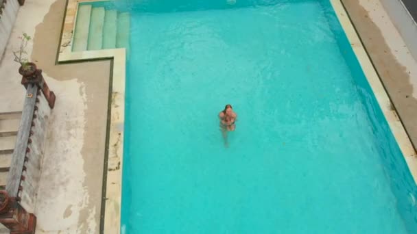 Filmagem aérea em câmera lenta de uma jovem mulher e seu filho turistas se divertindo em uma piscina em um ambiente tropical. Conceito de vida tropical — Vídeo de Stock