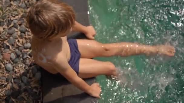 水泳プールで肩のスプラッシュ水に日焼け止めクリームで描かれた太陽と小さな男の子のスローモーションショット。太陽保護の概念 — ストック動画