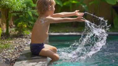 Omzuna güneş kremi sürmüş küçük bir çocuğun yüzme havuzuna su sıçrattığı yavaş çekim. Güneş koruma kavramı