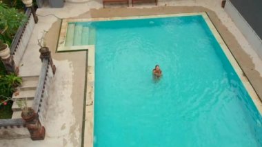 Genç bir kadın ve küçük oğlu turistlerin tropikal bir çevrede yüzme havuzunda iyi vakit geçirdikleri yavaş çekim. Tropikal yaşam konsepti