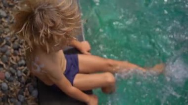 Omzuna güneş kremi sürmüş küçük bir çocuğun yüzme havuzuna su sıçrattığı yavaş çekim. Güneş koruma kavramı