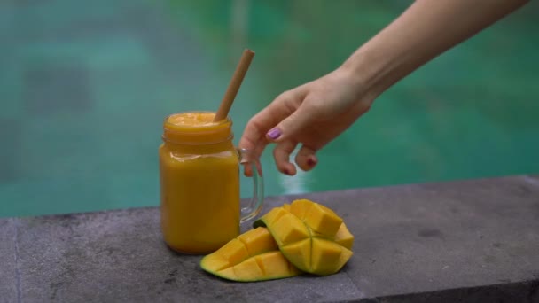 Gros plan d'un verre d'un shake à la mangue et couper des mangues sur un côté d'une piscine avec une paille de bambou à boire dedans. Alternative aux pailles en plastique. Concept de produits respectueux de l'environnement — Video