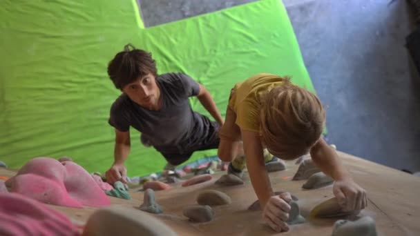 Een jonge man klimmen instructeur leren kleine jongen hoe de muur te beklimmen in een boulderend klimmen sportschool — Stockvideo