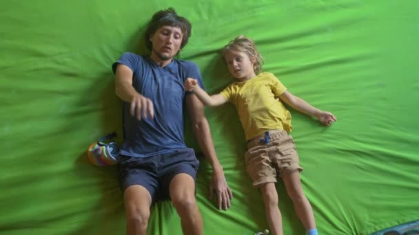 Молодий чоловік вчитель скелелазіння навчає маленького хлопчика, як піднятися на стіну в тренажерному залі для скелелазіння — стокове відео