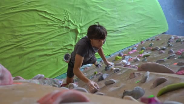 Joven hombre está escalando la pared en un gimnasio de escalada de rocas — Vídeos de Stock