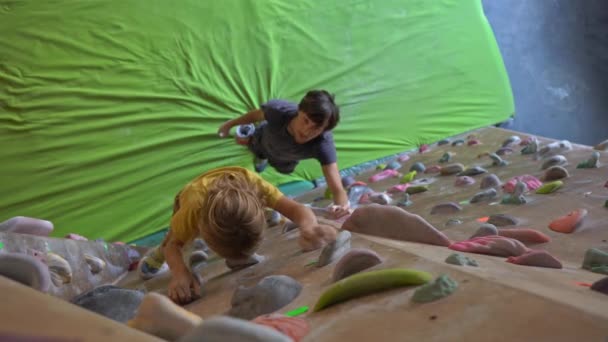 A young man climbing instructor teaching little boy how to climb the wall in a bouldering climbing gym — Stock Video