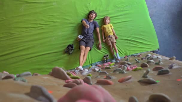 Un joven instructor de escalada enseñando a un niño a escalar la pared en un gimnasio de escalada — Vídeo de stock