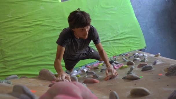 Young man is climbing the wall in a bouldering climbing gym — Stock Video