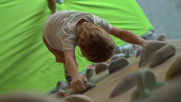 Маленький мальчик перелезает через стену в боулдеринговом спортзале — стоковое видео